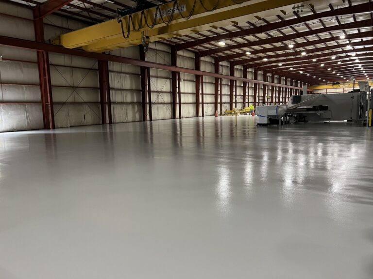 Wide view of a finished gray resinous floor in a steel fabrication bay with an overhead crane and machinery, American Steel and Aluminum, Auburn, MA