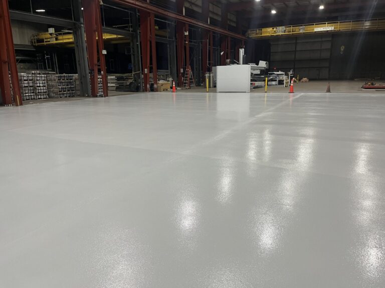 Finished gray resinous floor around a machine enclosure and storage racks, American Steel and Aluminum, Auburn, MA