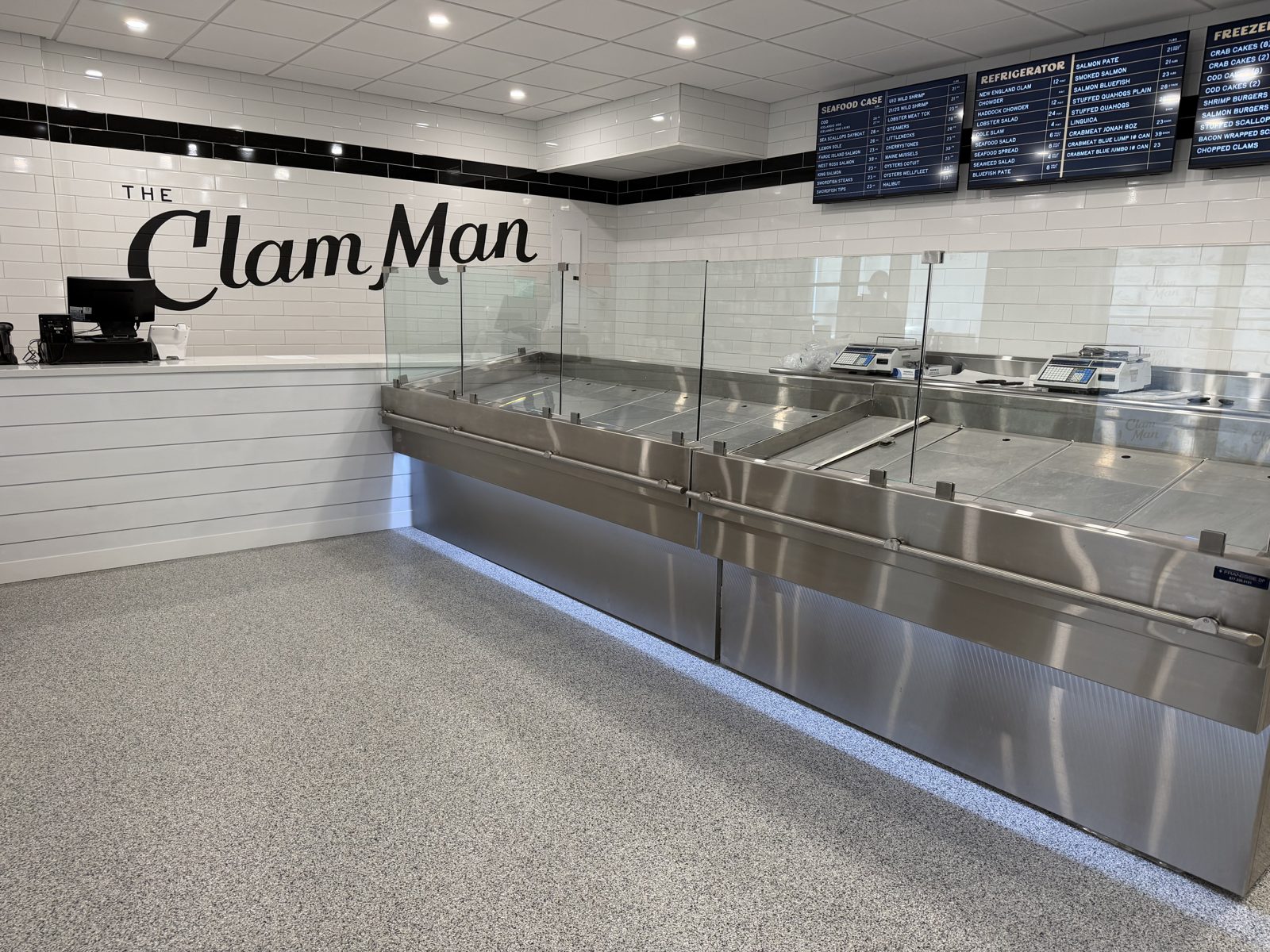 Gray flake epoxy floor in front of stainless steel seafood display cases and The Clam Man sign on a white tile wall