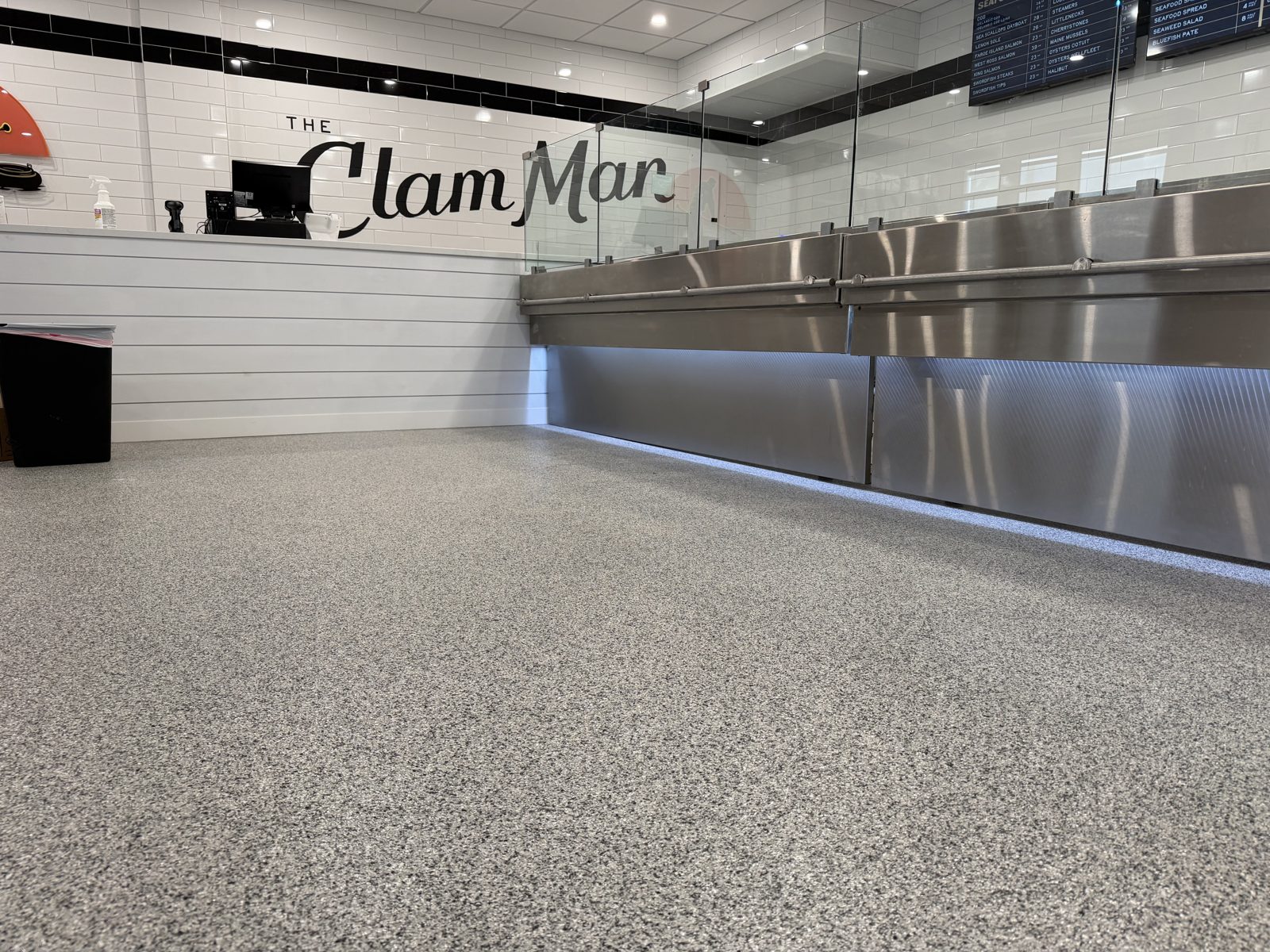 Low-angle view of a gray flake epoxy floor running along a lit stainless steel seafood counter
