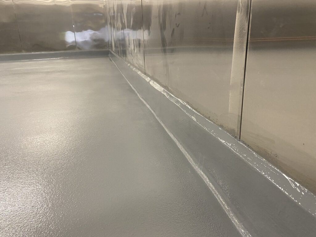 Gray epoxy floor with an integral cove base curving up a stainless steel wall