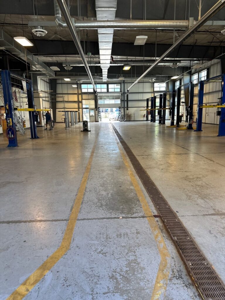 Worn automotive shop floor with trench drain and faded lines before work, Essex North Shore Agricultural & Technical School automotive shop, Danvers, MA
