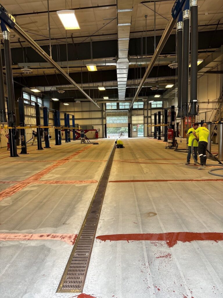 Automotive shop floor during preparation with trench drain and crew, Essex North Shore Agricultural & Technical School automotive shop, Danvers, MA
