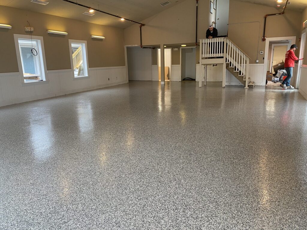 Glossy gray flake epoxy floor in a large room with white wainscoting, a staircase and two workers.