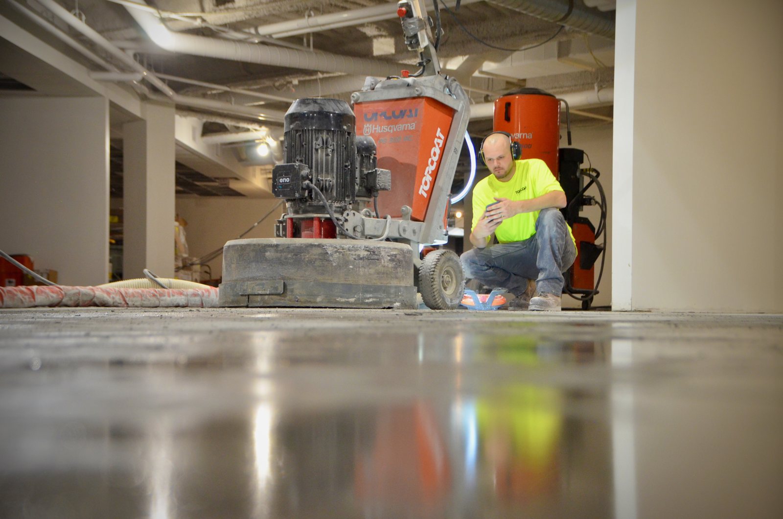 Topcoat crew member beside a diamond grinder with dust extraction on a concrete floor