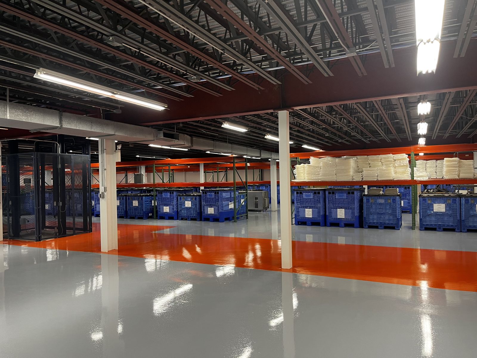 Glossy gray warehouse floor with an orange aisle beside racking and blue bins, High Purity New England, Smithfield, RI