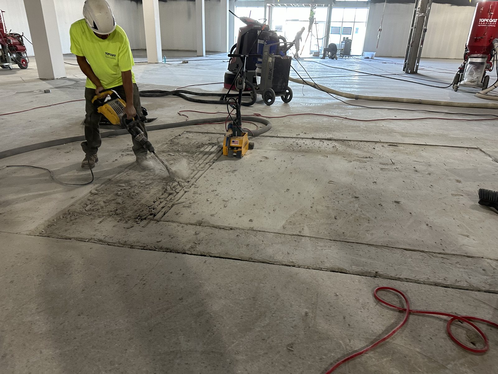 Crew member breaking out a saw-cut section of existing concrete floor with a breaker at L.L. Bean Outlet, Framingham