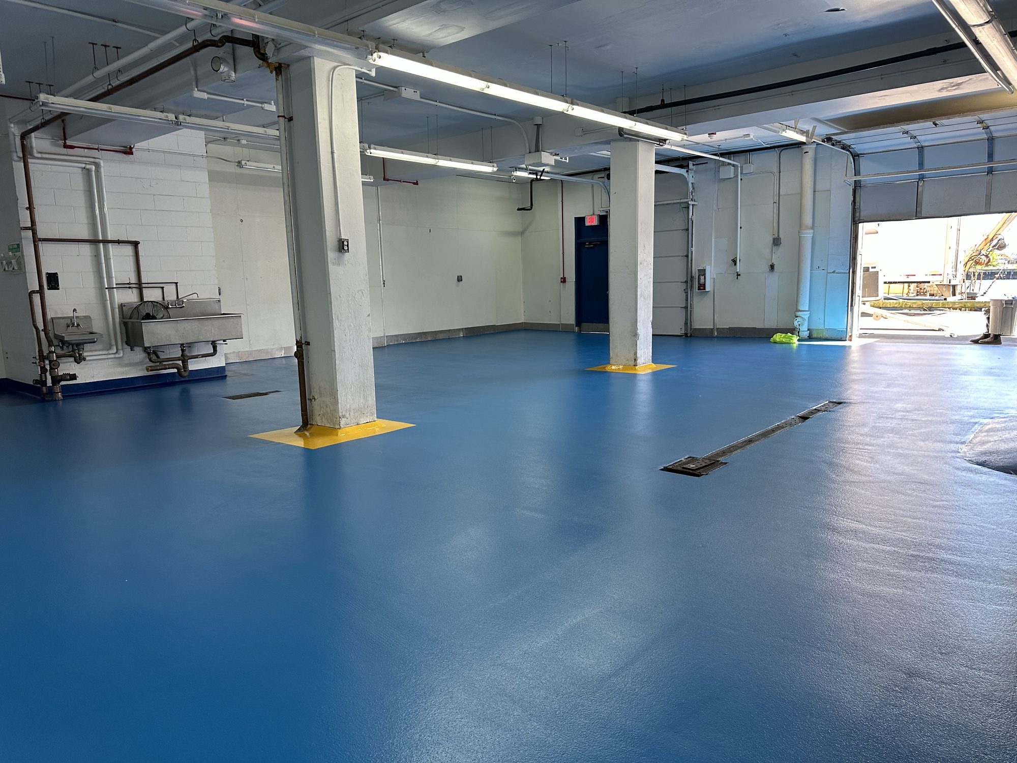 Open room with a two-tone blue floor, trench drain, columns with yellow bases and an open dock door, Rocky Neck Fish, Boston Fish Pier, Boston, MA