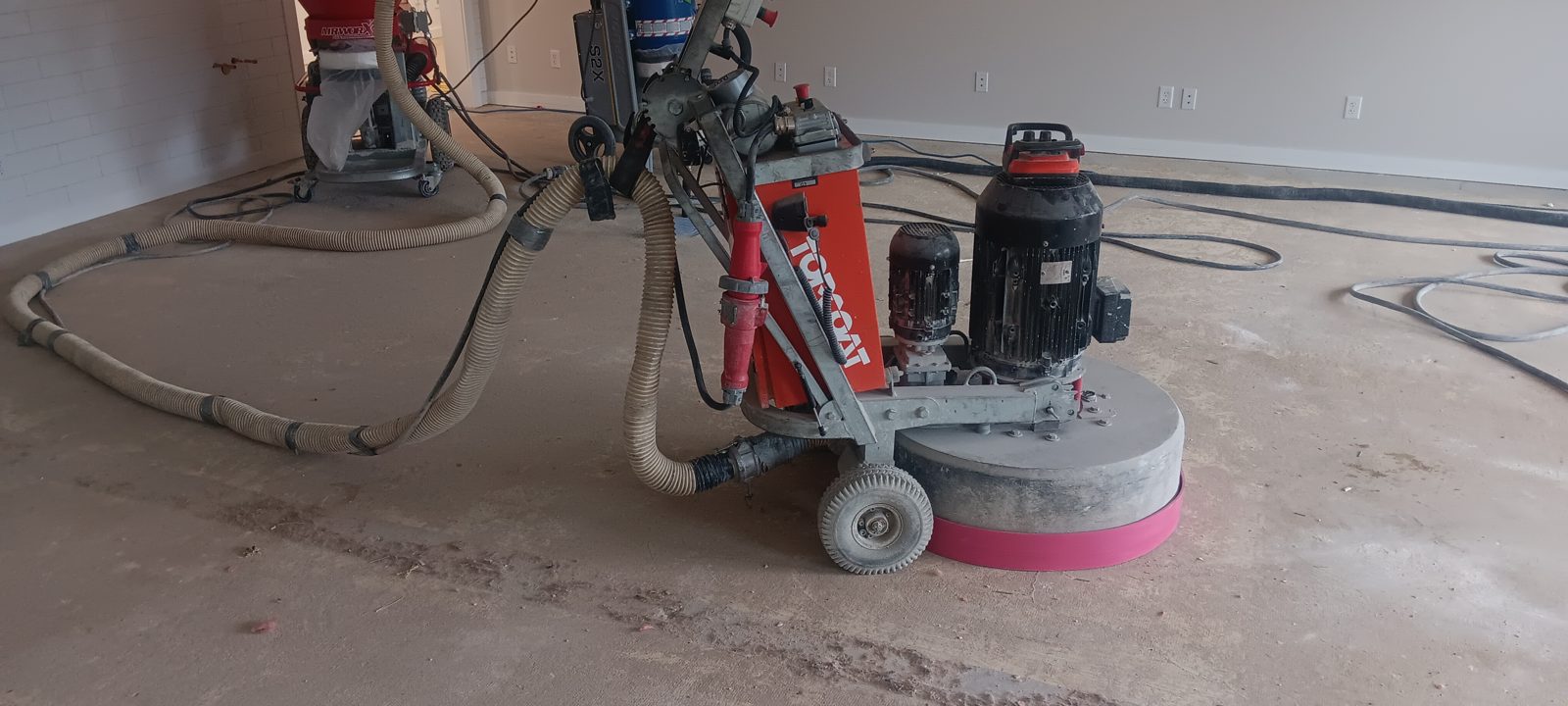 Topcoat floor grinder connected to dust collection hoses on a bare concrete slab