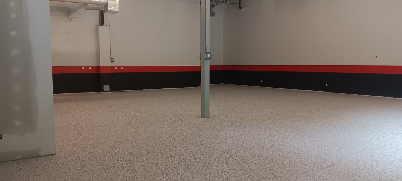 Finished light gray resinous floor in an open manufacturing facility with columns and red-and-black wall band, Telsonic, Westford, MA